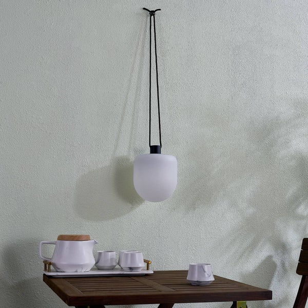 Moderne Hängeleuchte mit weißem, abgerundetem Schirm an einer schwarzen Kordel über einem Holztisch mit Teeservice.