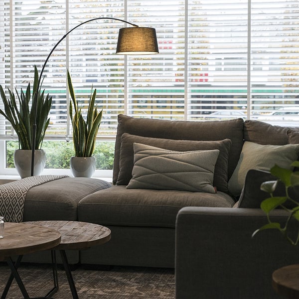 Wohnzimmer mit grauer Couch, Kissen, Stehlampe und Pflanzen