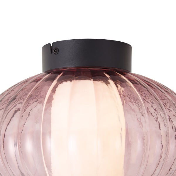 Nahaufnahme einer Deckenleuchte mit geripptem, rosa Glasschirm und schwarzer Metallhalterung.