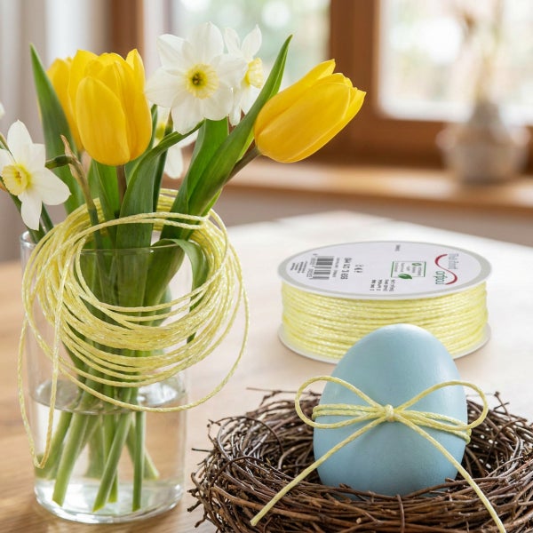 Eine Rolle Dekokordel mit Frühlingsblumen in einer Vase und einem Osterei in einem Nest als Dekoration für das Osterfest.