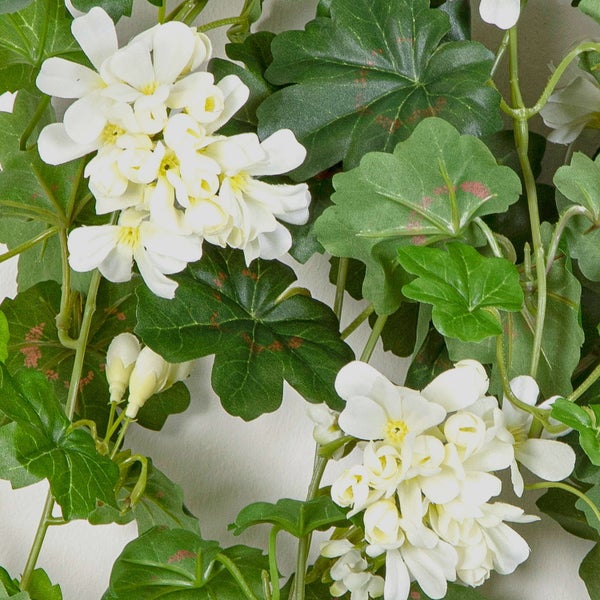 Künstliche Hängegeranie mit weißen Blüten und grünen Blättern.