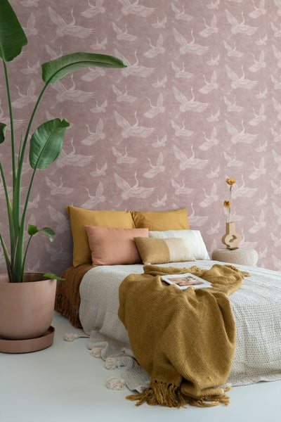 Schlafzimmer mit Bett, Kissen, Tagesdecke, Pflanze und Wandtapete mit Vogelmuster für eine ruhige Atmosphäre