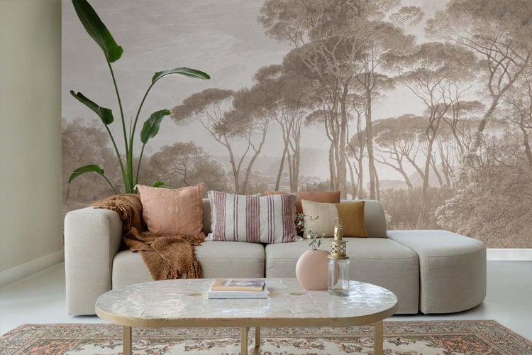 Wohnzimmer mit einer Fototapete mit Waldlandschaft in Sepiatönen, einem beigen Sofa mit Kissen und einer großen Zimmerpflanze.