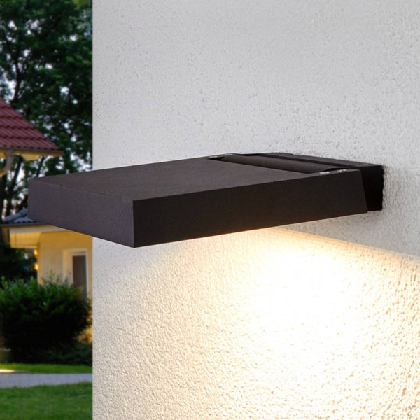 Moderne LED-Außenwandleuchte in Schwarz, flaches rechteckiges Design, Lichtstrahl nach unten auf eine strukturierte Hauswand gerichtet.