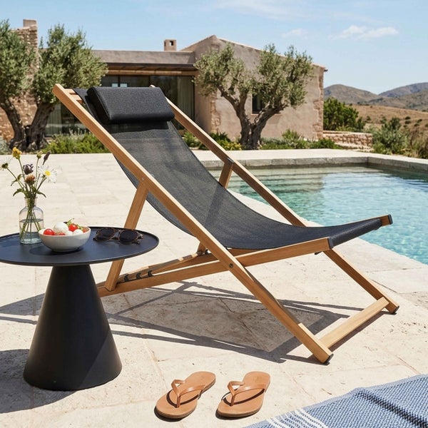 Gartenliege aus Holz mit schwarzer Textilbespannung und Kopfkissen auf einer Steinterrasse am Pool neben einem Beistelltisch.