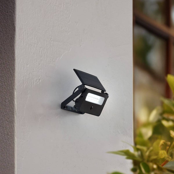 Schwarzer LED-Solarstrahler mit Bewegungsmelder an einer weißen Hauswand montiert.