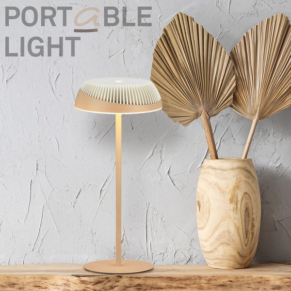 Moderne, tragbare LED-Tischleuchte mit plissiertem Design auf einer Holzoberfläche neben einer Holzvase mit getrockneten Palmblättern.