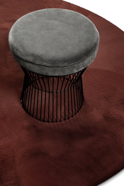 Grauer Samthocker mit schwarzem Metallgestell auf einem weichen Teppich.