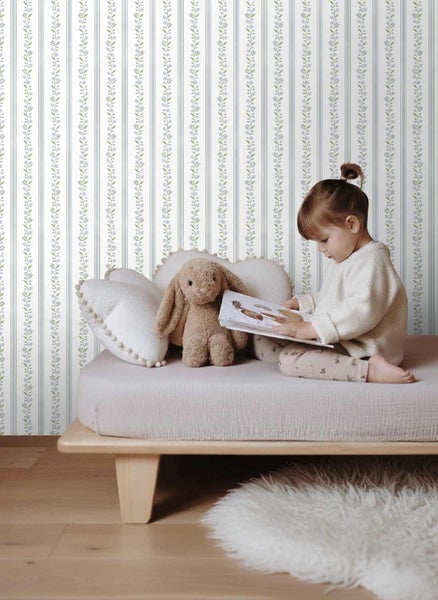 Tapete mit blauem Streifenmuster und floralen Ranken in einem hellen Kinderzimmer mit Holzbett.