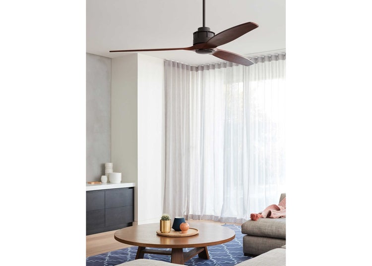 Moderner Deckenventilator mit drei Holzflügeln, montiert an einer hellen Wohnzimmerdecke über einem runden Holztisch und einem Sofa.