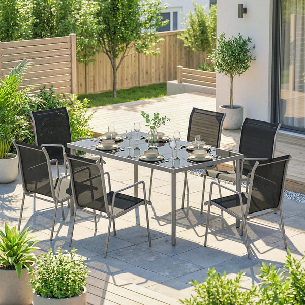Gartensitzgruppe mit rechteckigem Tisch aus Metall und Glas sowie sechs Gartenstühlen mit schwarzem Textilgewebe auf einer hellen Terrasse.