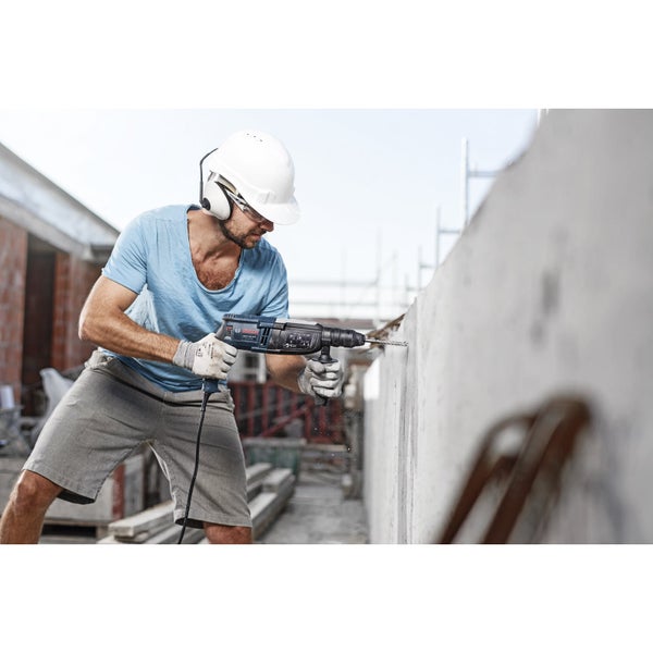 Handwerker bohrt mit einer Schlagbohrmaschine ein Loch in eine Betonwand. Er trägt Schutzhelm und Gehörschutz.