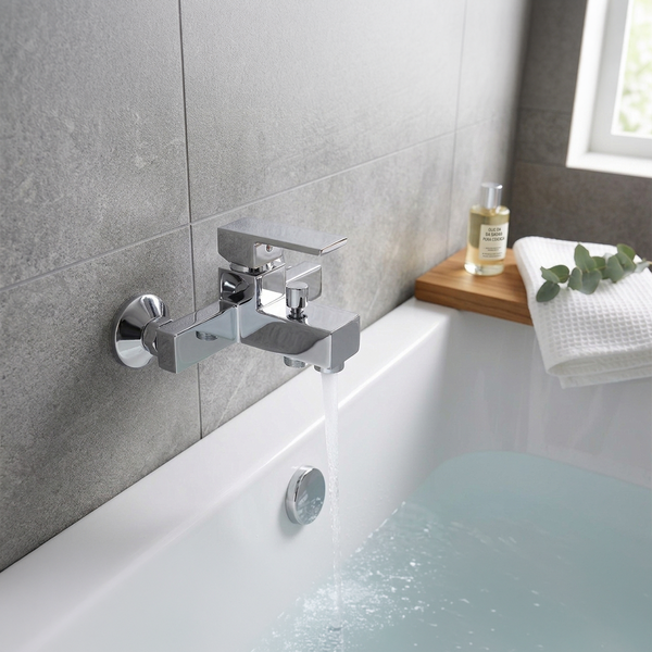 Moderne, verchromte Wannenarmatur in eckigem Design für Wandmontage mit Einhebelmischer an einer Badewanne mit grau gefliester Wand.
