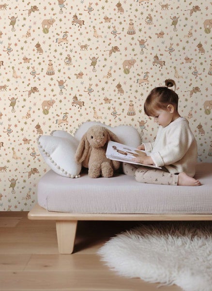 Ein Kind liest ein Buch auf einem Bett vor einer Kindertapete mit Zirkusmotiven wie Tieren und Sternen im Kinderzimmer.