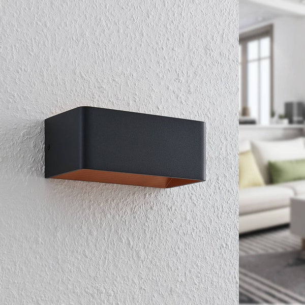 Wandleuchte in Schwarz mit kupferfarbener Innenseite an einer weiß strukturierten Wand.