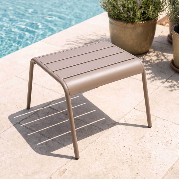 Moderner Gartenhocker oder Beistelltisch aus Metall mit Lattenoberfläche auf einer hellen Terrasse am Pool.