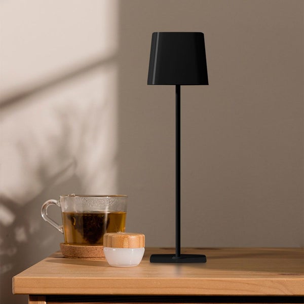 Schwarze Tischleuchte neben einem Glas Tee auf einem Tisch