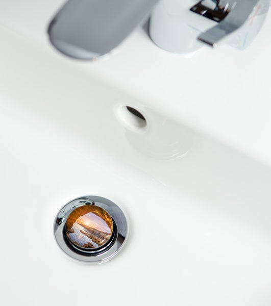 Detailansicht eines weißen Waschbeckens mit glänzendem Wasserhahn und Abflussstopfen