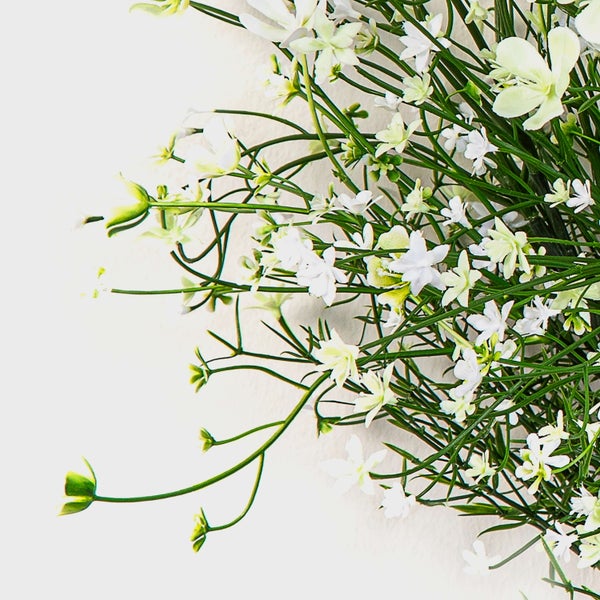 Künstliche Dekopflanze mit kleinen weißen Blüten an feinen grünen Verzweigungen.