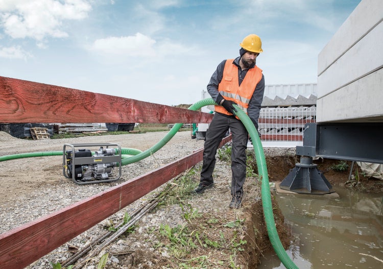 Bauarbeiter nutzt Kärcher Benzin-Schmutzwasserpumpe mit Saugschlauch auf einer Baustelle zum Abpumpen von Wasser aus einer Grube.