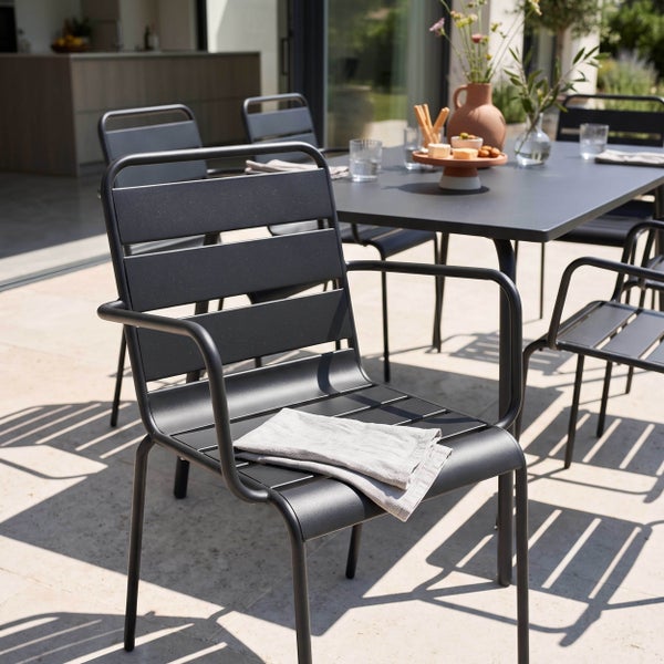 Modernes Gartenmöbel-Set aus schwarzen Metallstühlen mit Armlehnen und einem Esstisch auf einer hellen, organisierten Terrasse.