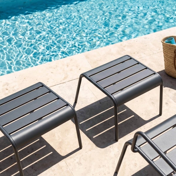 Zwei moderne Gartenhocker aus anthrazitfarbenem Metall mit Lattenstruktur auf einer Steinterrasse am Pool.
