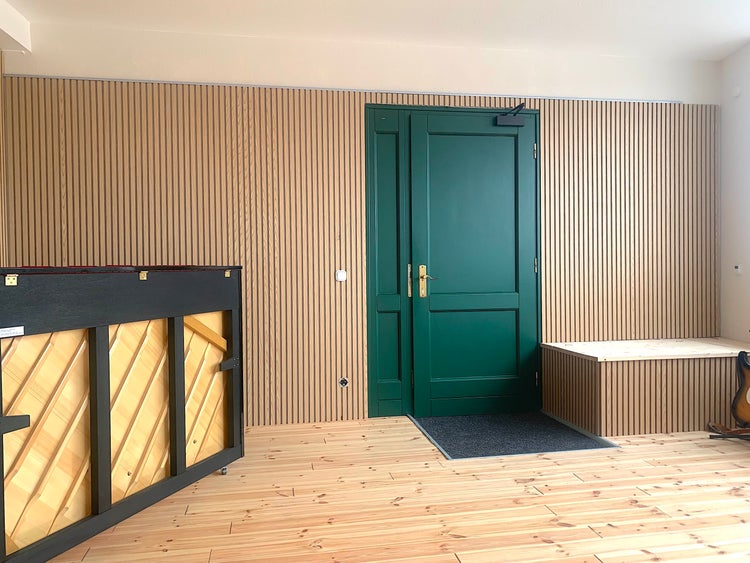 Moderner heller Raum mit Wandpaneelen aus Holzlamellen, einer grünen Tür und hellem Holzboden.