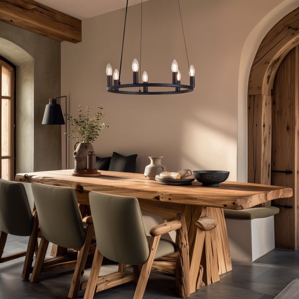 Rustikales Esszimmer mit großem Holztisch, gepolsterten Stühlen und einem runden, schwarzen Kronleuchter als Lichtquelle.