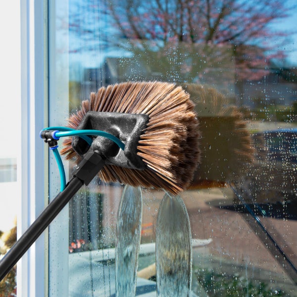 Waschbürste mit Teleskopstiel zur Fensterreinigung beim Reinigen einer Fensterscheibe mit austretendem Wasserstrahl