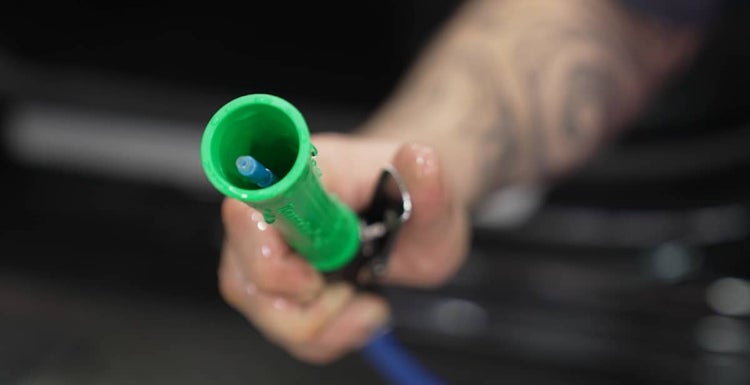 Eine Hand hält einen grünen Gartenschlauch mit blauem Anschlussstück.