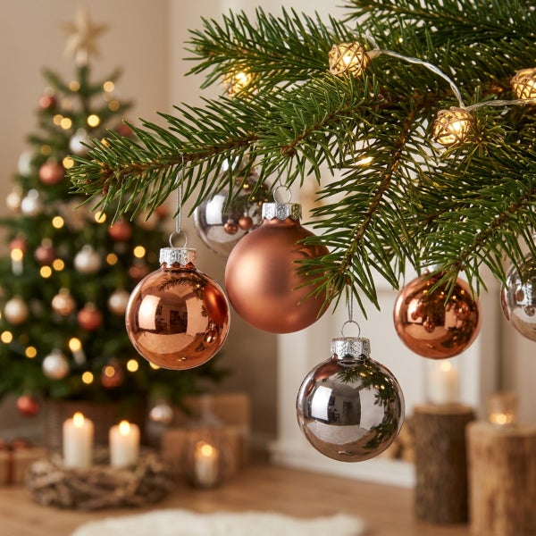 Weihnachtsbaumkugeln hängend an einem Tannenbaum mit Lichterkette im festlich dekorierten Wohnzimmer.