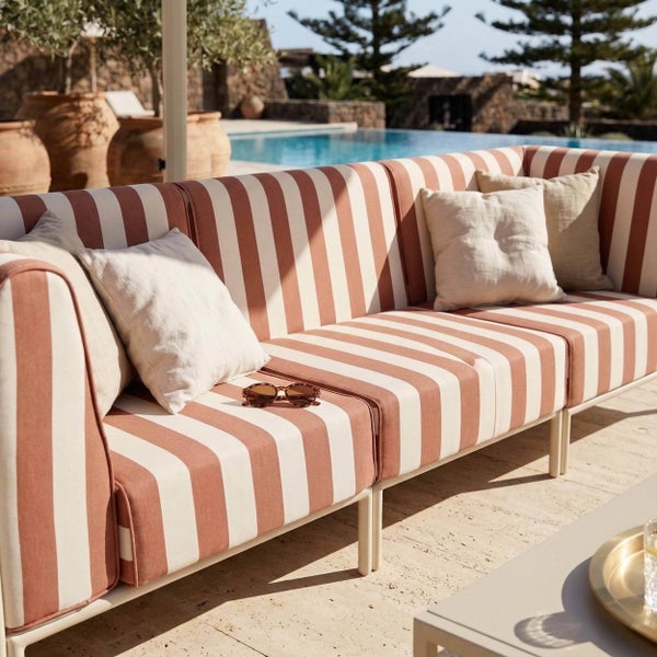 Gestreiftes Outdoor-Lounge-Sofa mit hellen Kissen auf einer Steinterrasse am Pool, helle und strukturierte Atmosphäre.