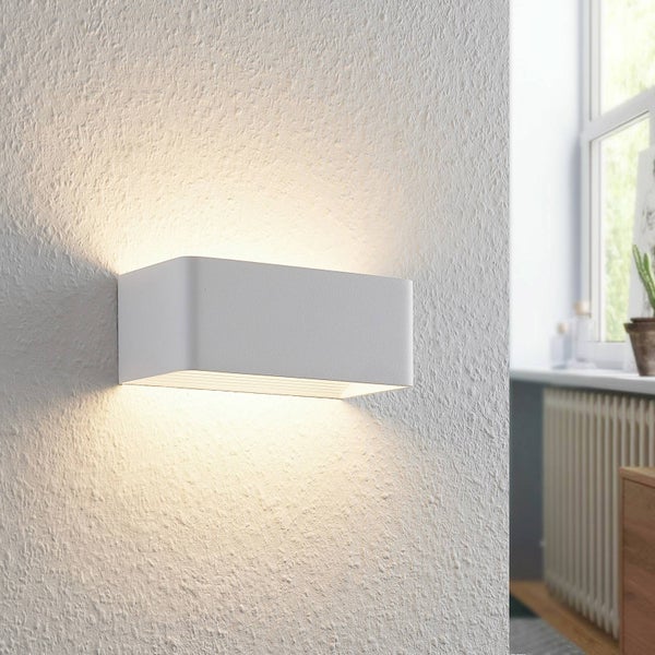 Moderne rechteckige Wandleuchte mit abgerundeten Ecken, strahlt Licht nach oben und unten auf eine strukturierte Wand in einem hellen Raum.