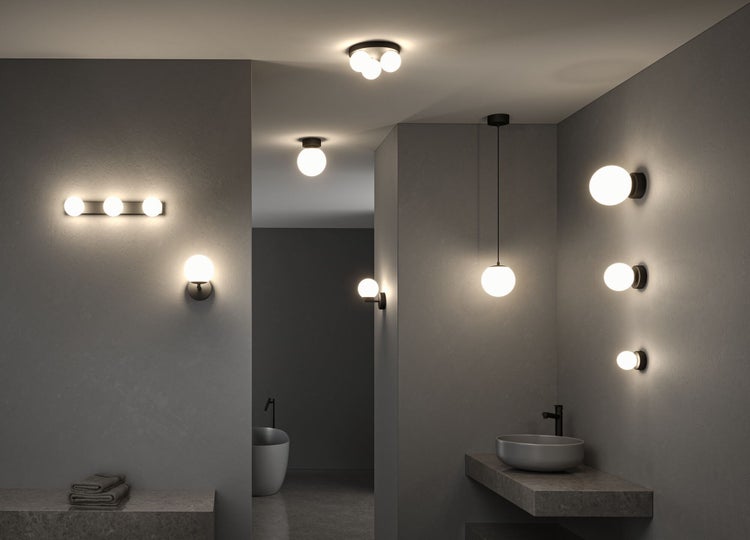 Modernes Badezimmer mit kugelförmigen Leuchten, wie Wand-, Decken- und Pendellampen aus Glas mit schwarzen Halterungen in Steinoptik-Umgebung.