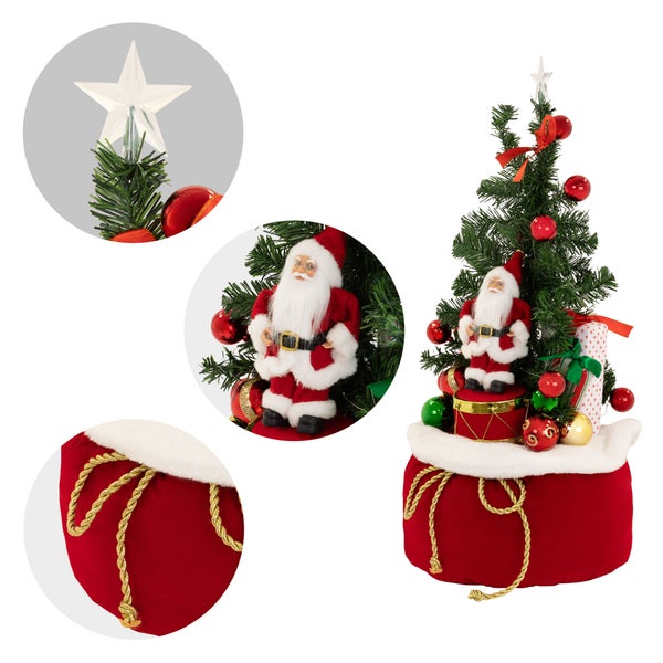 Künstlicher Weihnachtsbaum in einem Geschenksack mit Santa Figur, Dekokugeln, einer Sternspitze und einer Geschenkschachtel als Weihnachtsdeko.