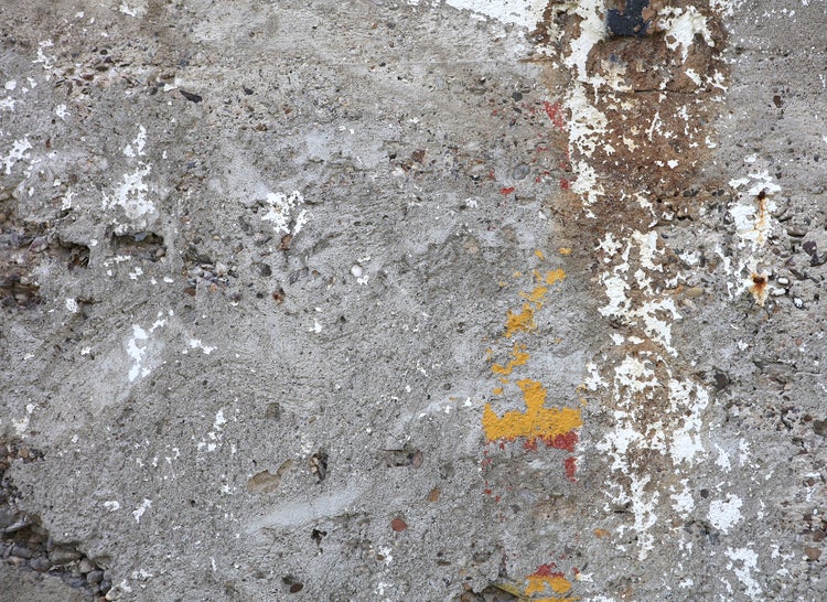 Stark verwitterte Betonwand mit Resten von abblätternder Farbe und sichtbarem Kies.