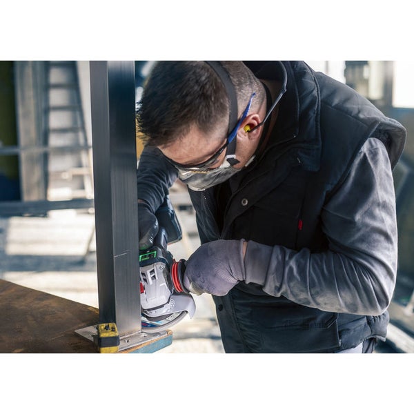 Ein Mann schleift mit einer Flex ein Metallstück, wobei er Schutzbrille, Gehörschutz und Staubmaske trägt.