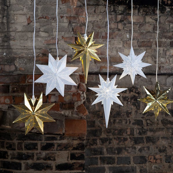 Mehrere beleuchtete Papiersterne in Gold und Weiß hängen vor einer Ziegelwand und erzeugen eine festliche Atmosphäre.