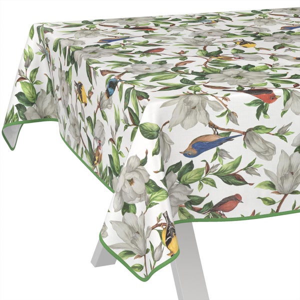 Weiße Tischdecke mit botanischem Muster aus Magnolienblüten, grünen Blättern und bunten Vögeln sowie einem grünen Rand.