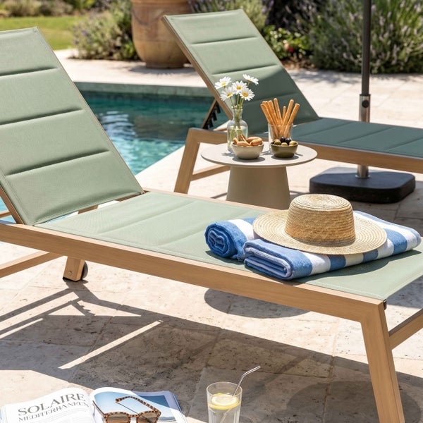 Zwei moderne Sonnenliegen aus Aluminium und Textilgewebe auf einer Terrasse am Pool mit Beistelltisch und Sommer-Accessoires.