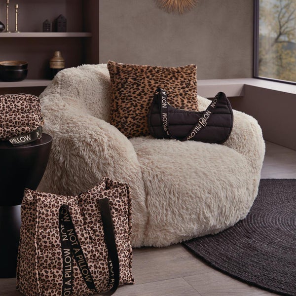 Gemütliches Wohnzimmer mit flauschigem Sessel, Kissen im Leopardenmuster und verschiedenen gesteppten Taschen.