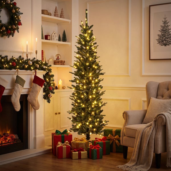 Schlanker künstlicher Weihnachtsbaum mit integrierter LED Beleuchtung in einem weihnachtlich geschmückten Wohnzimmer mit Kamin und Geschenken.