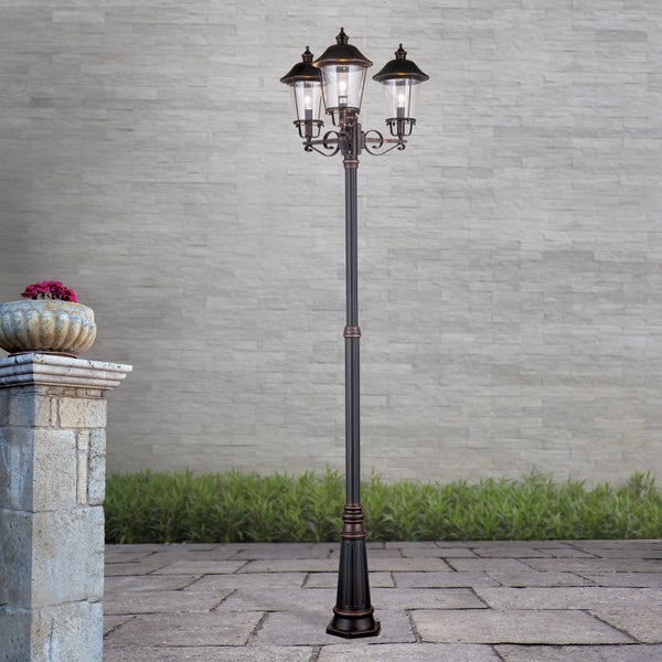 Dreiflammige Außenstehleuchte im klassischen Laternen-Design auf einer gepflasterten Terrasse vor einer Steinwand.