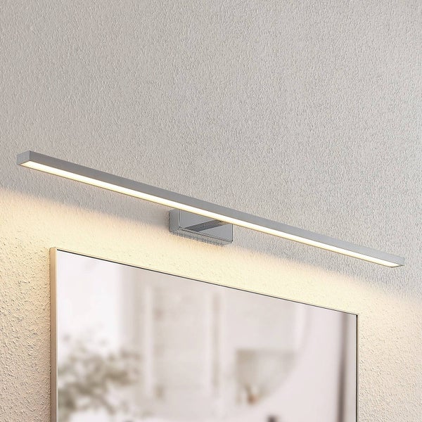 Moderne LED Spiegelleuchte über einem Wandspiegel montiert, Gehäuse in Chrom Optik, warmweißes Licht strahlt auf die strukturierte Wand.