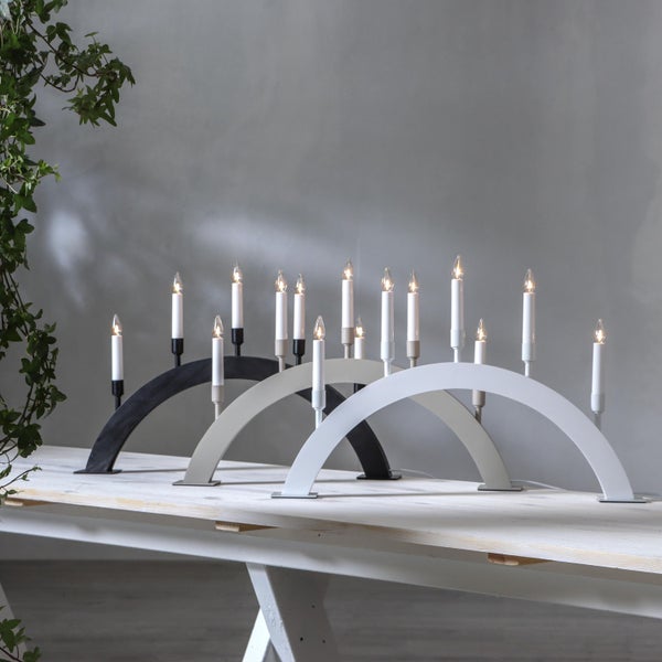 Drei skandinavische Adventsleuchter mit Bogenform und elektrischen Kerzen auf einem Tisch.