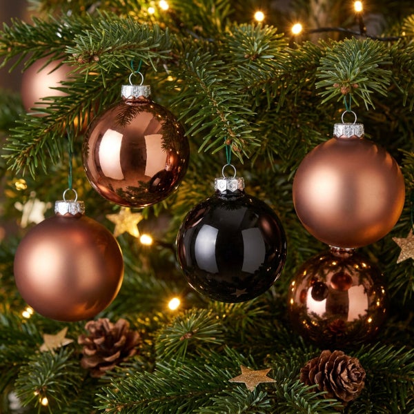 Weihnachtsbaumkugeln in verschiedenen Oberflächen hängend an einem Tannenbaum mit Lichterkette und Tannenzapfen.