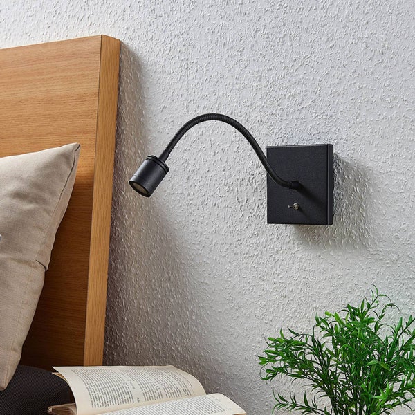 Schwarze Wandleseleuchte mit flexiblem Arm und Kippschalter, montiert an einer strukturierten Wand neben einem Bett.