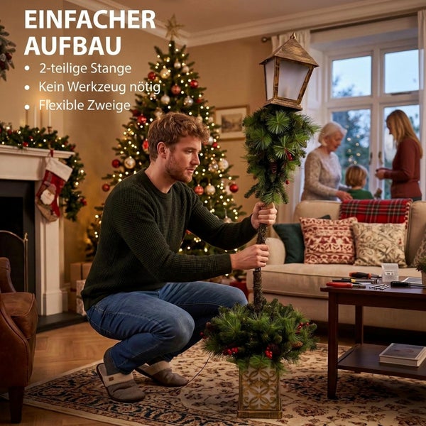 Mann montiert künstliche Weihnachtsstraßenlaterne mit Tannenzweigen in einem gemütlichen Wohnzimmer vor einem geschmückten Weihnachtsbaum.