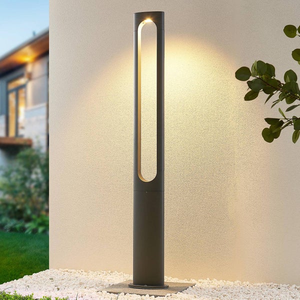 Moderne LED-Wegleuchte in Anthrazit vor einer hellen Wand im Außenbereich, stehend auf weißen Steinen.