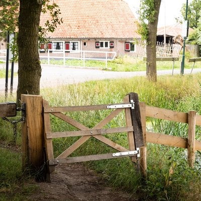 Rustikales Holztor für den Garten mit Kreuzstrebe und Scharnieren aus Metall in einer ländlichen Umgebung.